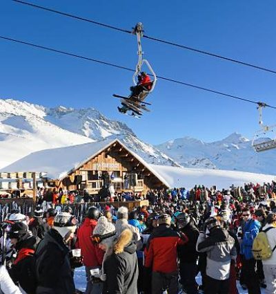 Val Thorens, France - January 22, 2013: People having a drink at the popular La Folie Douce bar at the ski piste near Val Thorens on a beautiful sunny day. Skiers are sitting in the overhead chair lift.